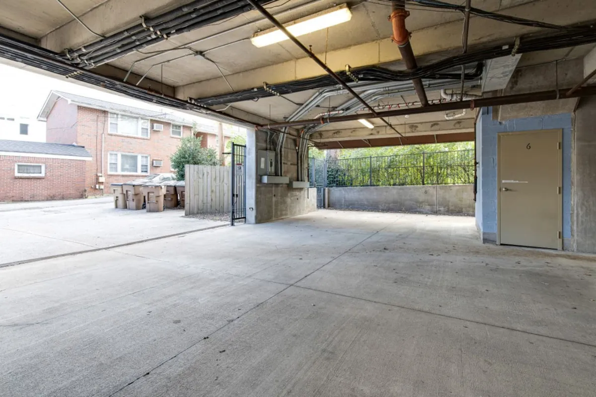A secure indoor garage space featuring exposed ceiling pipes, concrete flooring, a visible security gate, and a numbered door (Door 6). The area is well-lit and organized, illustrating both safety and ease of access for parking vehicles or storing bikes.