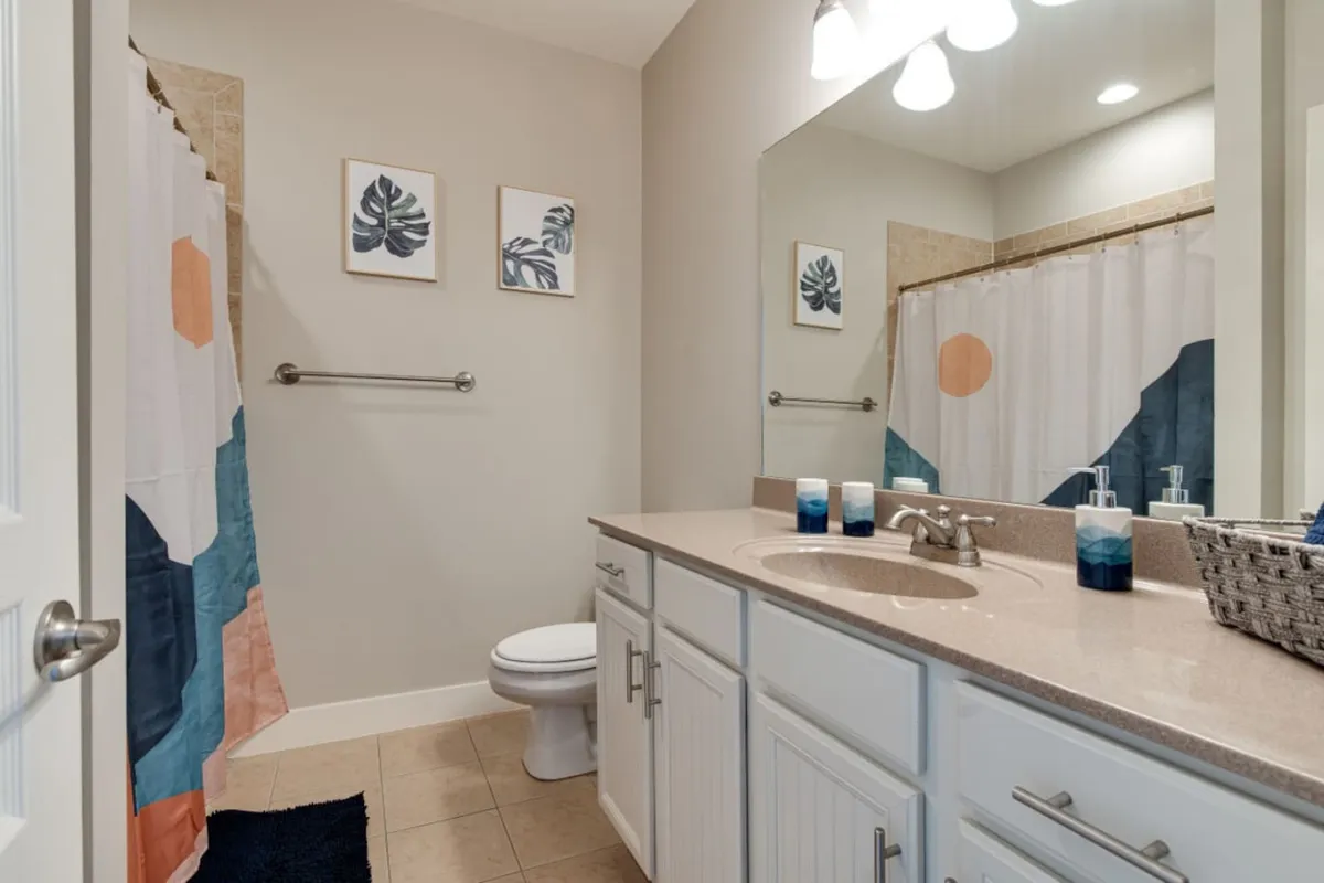 A modern bathroom scene with a vanity and sink, a colorful shower curtain, and framed wall art. The space is bright and fresh, designed for rejuvenation and comfort, reflecting a modern en-suite bathroom experience.