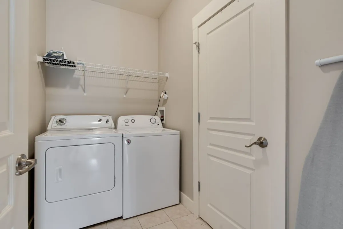 A tidy laundry nook featuring a washer and dryer set beneath a shelf, with cleaning supplies neatly stored above. The area is bright and organized, evoking a sense of efficiency and home-like convenience.