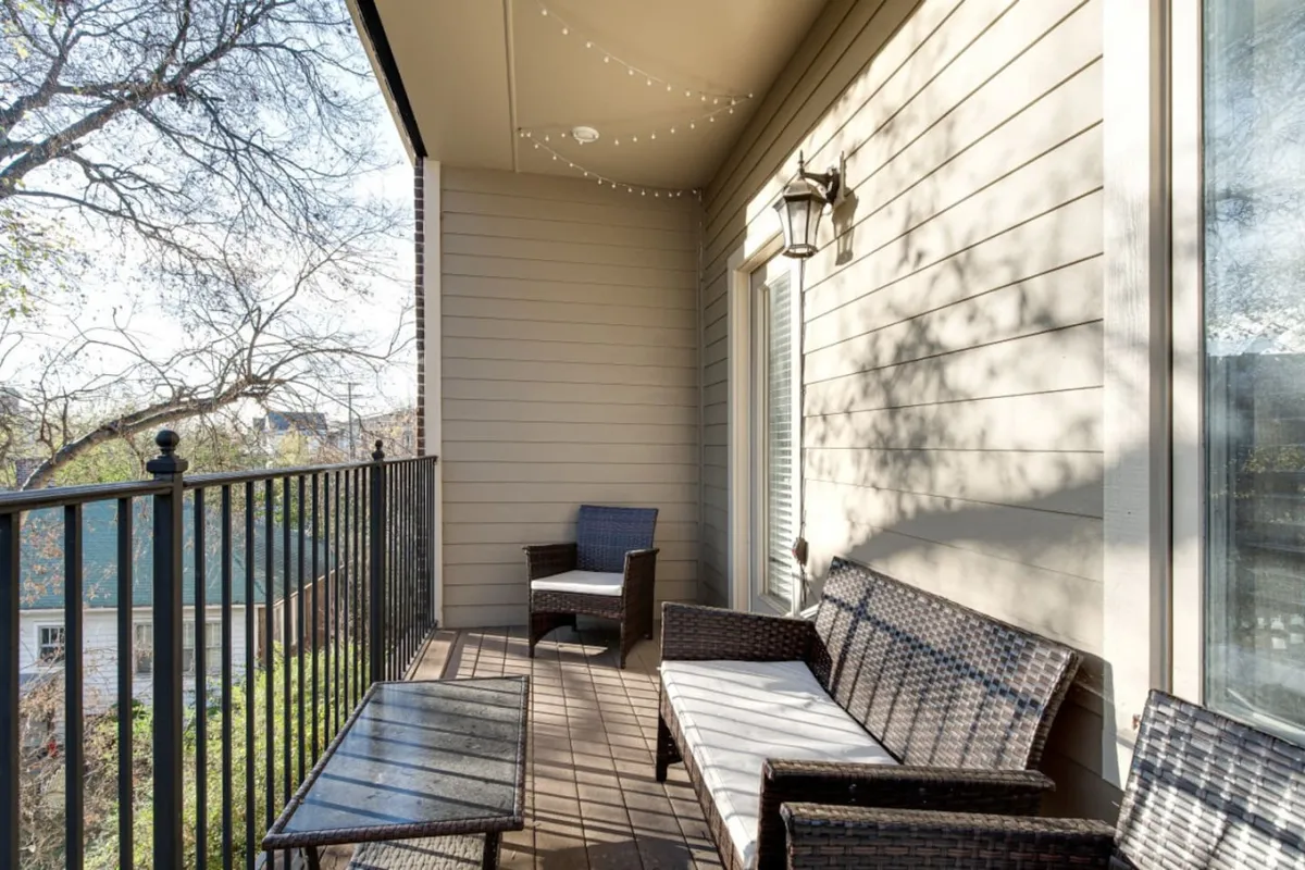 The image showcases the condo's inviting outdoor space, featuring cozy wicker seating beneath glowing string lights on a private balcony. The tranquil setting hints at a perfect spot for relaxing, enjoying a morning coffee, or unwinding with friends while taking in sunset views.