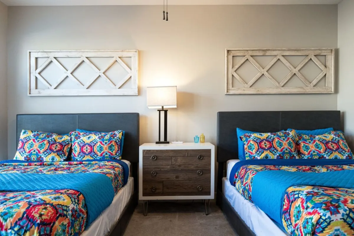 A cozy, cheerful dining and bedroom area with colorful bedspreads, a nightstand with a lamp, and framed wall art, creating a welcoming space for relaxing and enjoying meals or conversations together.